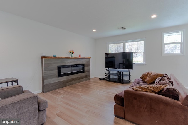 living room with a healthy amount of sunlight, a tiled fireplace, light wood-style floors, and visible vents