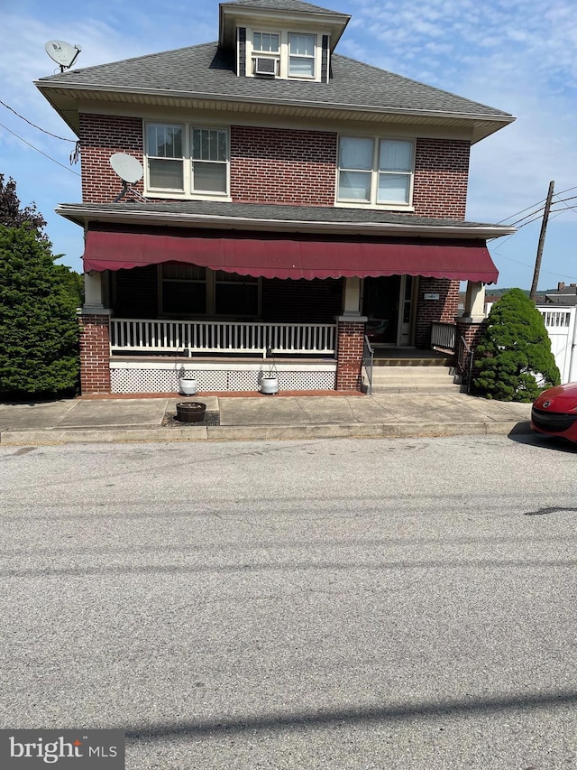 view of front of home featuring roof with shingles, a porch, and brick siding