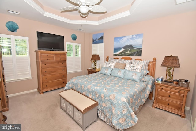 bedroom featuring a ceiling fan, a tray ceiling, baseboards, visible vents, and light colored carpet