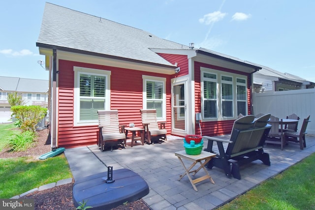 rear view of house with a patio, roof with shingles, and fence