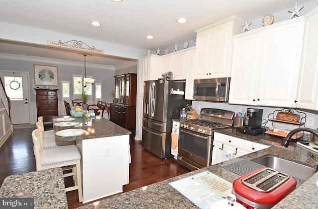 kitchen with a chandelier, crown molding, a kitchen island, stainless steel appliances, and dark stone counters