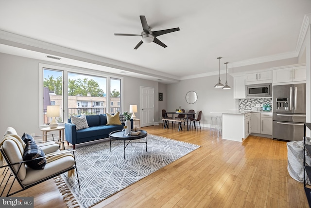 living room with visible vents, crown molding, baseboards, ceiling fan, and light wood finished floors