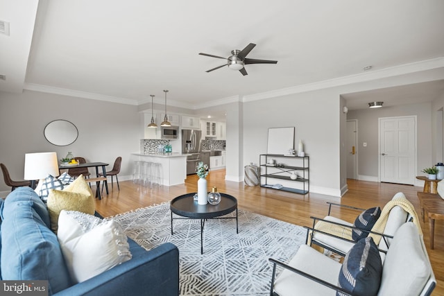 living room with crown molding, a ceiling fan, baseboards, and light wood-style flooring