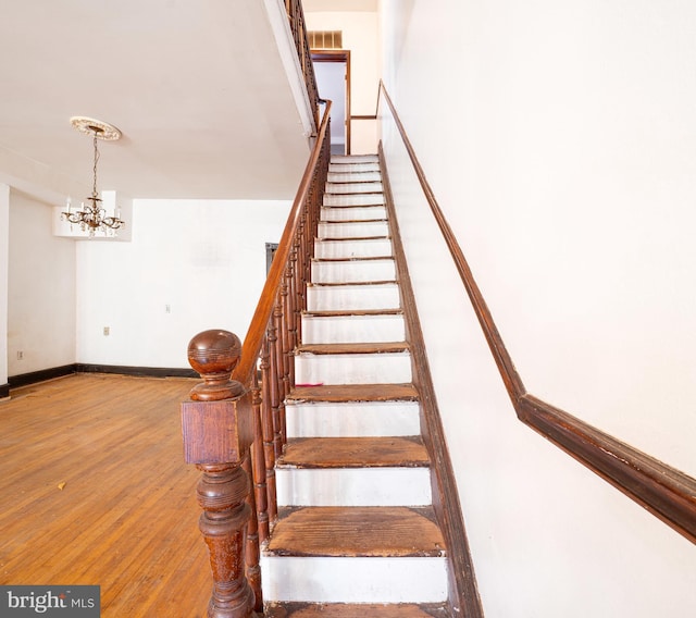 staircase featuring wood finished floors, a chandelier, and baseboards