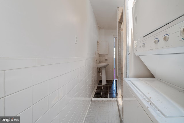 washroom with stacked washing machine and dryer, tile patterned floors, and tile walls