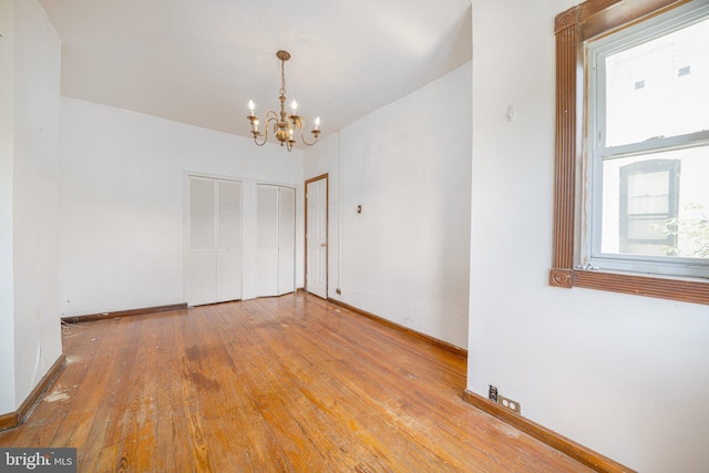 spare room featuring a chandelier, hardwood / wood-style flooring, and baseboards