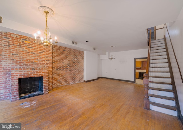 unfurnished living room with a chandelier, hardwood / wood-style floors, stairway, a brick fireplace, and brick wall