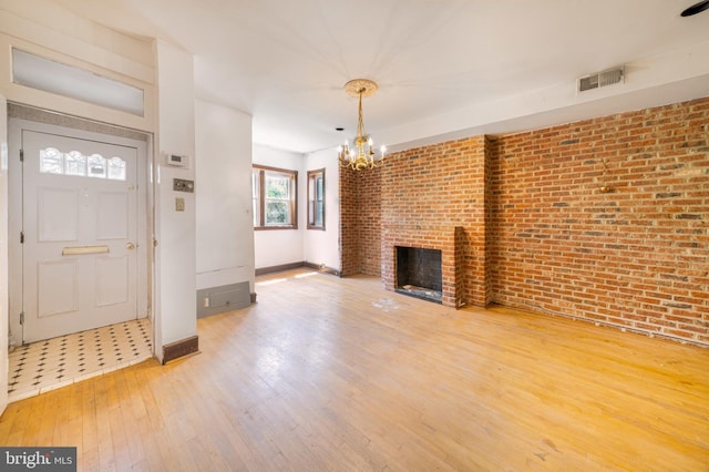 unfurnished living room with a chandelier, hardwood / wood-style floors, baseboards, brick wall, and a brick fireplace