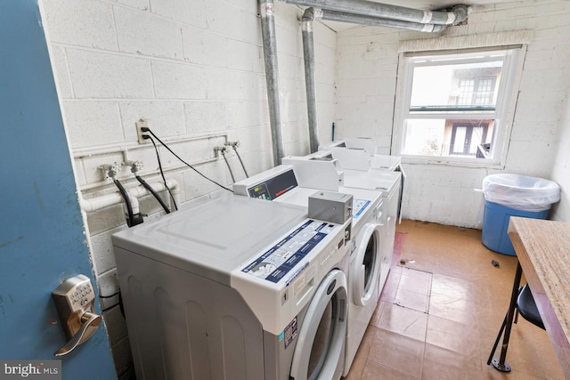clothes washing area with washing machine and clothes dryer and concrete block wall