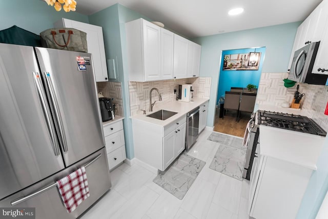 kitchen with appliances with stainless steel finishes, a sink, light countertops, baseboards, and decorative backsplash