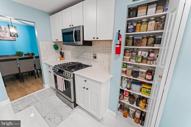 kitchen with decorative backsplash, baseboards, light countertops, white cabinets, and stainless steel appliances
