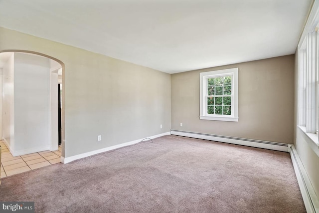 carpeted empty room featuring arched walkways, baseboards, a baseboard heating unit, and tile patterned floors