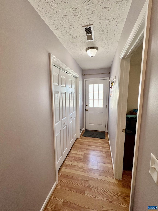 doorway to outside featuring light wood-style floors, baseboards, a textured ceiling, and visible vents