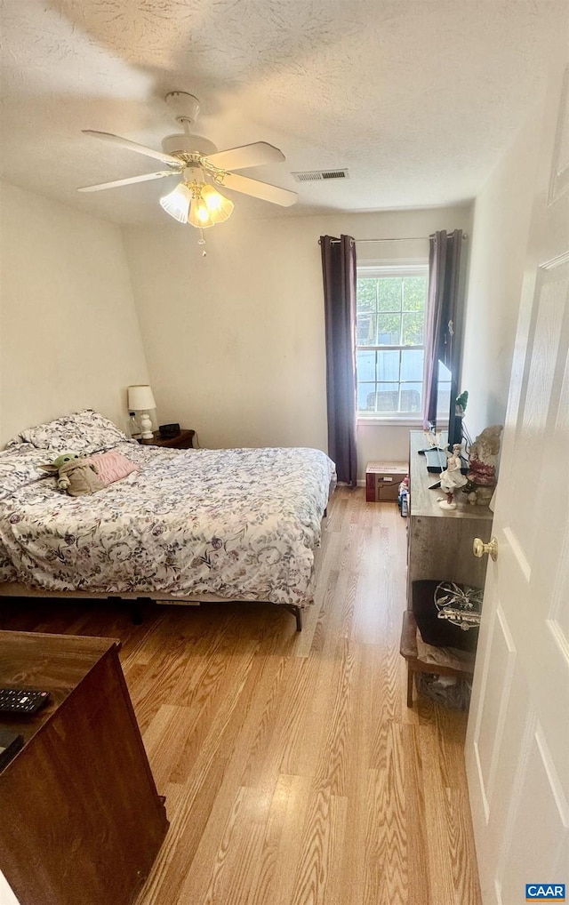 bedroom featuring visible vents, a ceiling fan, light wood finished floors, and a textured ceiling