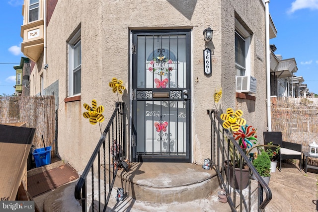 view of exterior entry with fence and stucco siding