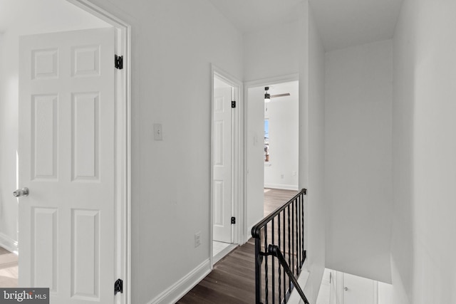 corridor with baseboards, dark wood-style flooring, and an upstairs landing