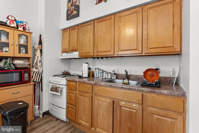 kitchen with dark countertops, white gas range oven, a sink, wood finished floors, and under cabinet range hood
