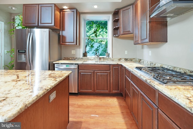 kitchen featuring appliances with stainless steel finishes, light stone counters, a sink, light wood finished floors, and under cabinet range hood