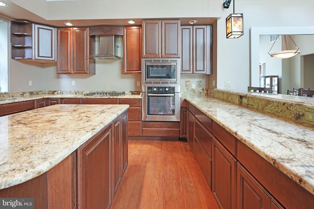 kitchen featuring light wood-type flooring, light stone counters, wall chimney range hood, and stainless steel appliances