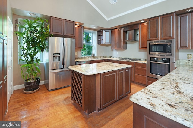 kitchen with wall chimney range hood, crown molding, appliances with stainless steel finishes, light wood-style flooring, and vaulted ceiling