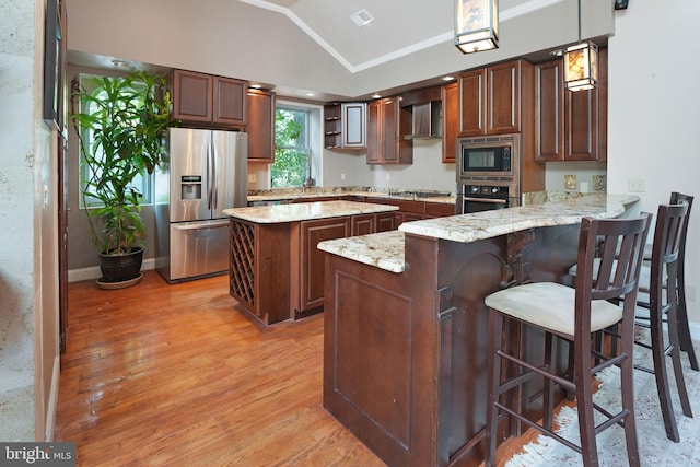 kitchen with a peninsula, wall chimney range hood, light wood-style flooring, vaulted ceiling, and stainless steel appliances