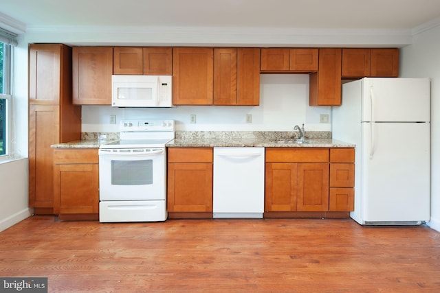kitchen with white appliances, brown cabinetry, ornamental molding, and a sink