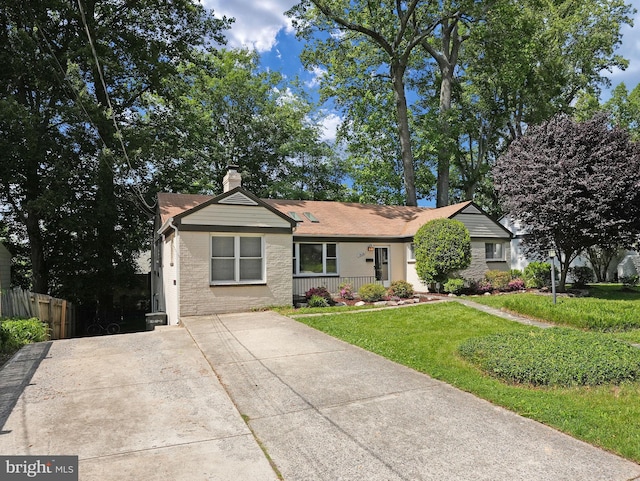 view of front of house with fence, brick siding, a porch, a front yard, and a chimney