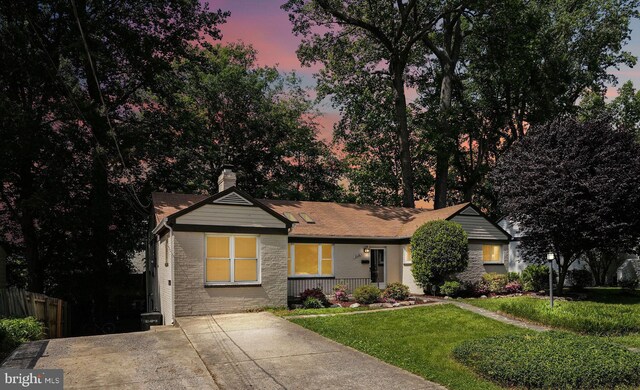 ranch-style home with covered porch, a chimney, a front yard, brick siding, and fence