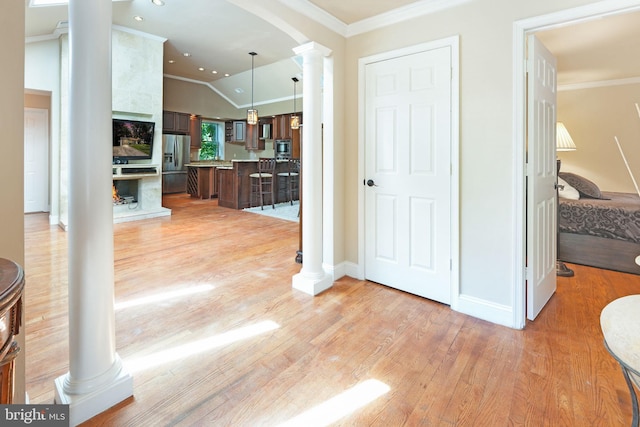 hall featuring light wood-style floors, ornamental molding, decorative columns, and vaulted ceiling