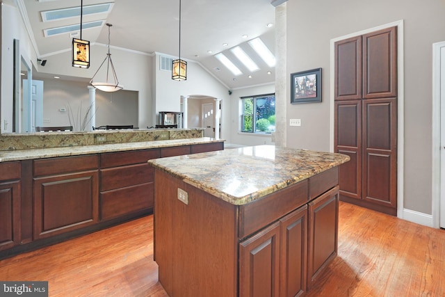 kitchen with light wood-style floors, arched walkways, vaulted ceiling, and ornamental molding