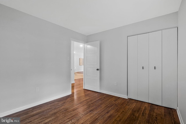 unfurnished bedroom with dark wood finished floors, a closet, and baseboards