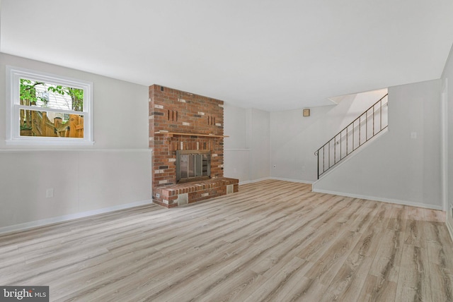 unfurnished living room with wood finished floors, stairs, baseboards, and a brick fireplace
