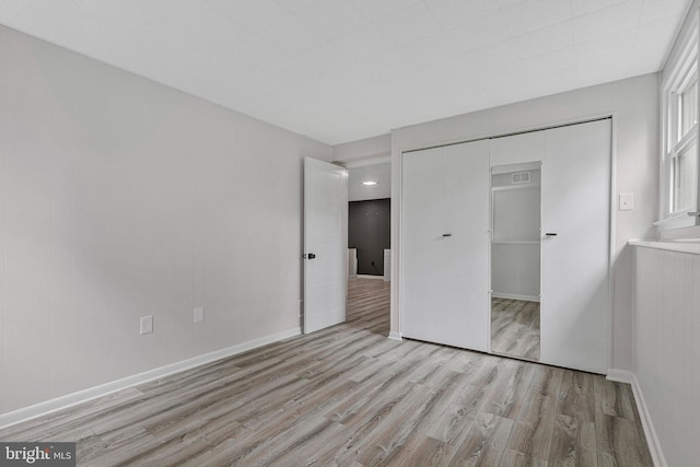 unfurnished bedroom with light wood finished floors, baseboards, and a closet