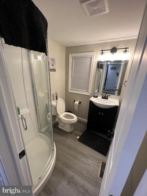 bathroom with vanity, toilet, a shower stall, wood finished floors, and visible vents