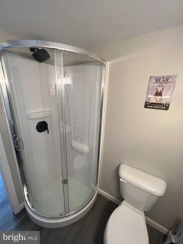 full bath featuring toilet, baseboards, wood finished floors, and a stall shower