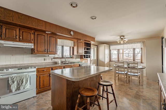 kitchen featuring a sink, a breakfast bar, under cabinet range hood, ceiling fan, and white range with electric stovetop