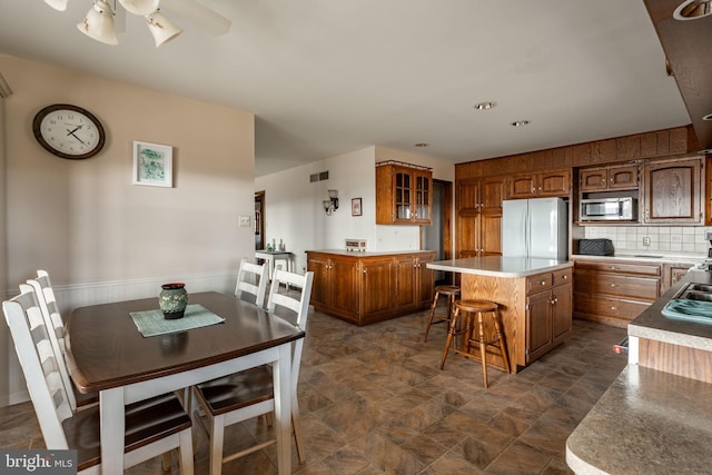 kitchen with stainless steel microwave, brown cabinets, freestanding refrigerator, ceiling fan, and a center island