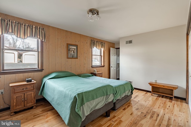 bedroom featuring light wood-type flooring, baseboards, wood walls, and visible vents