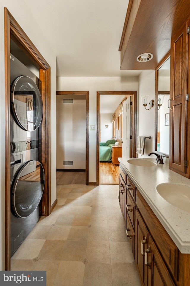 bathroom with a sink, double vanity, stacked washer / dryer, and visible vents