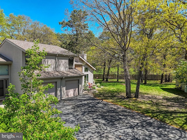 view of side of property with fence, an attached garage, aphalt driveway, a chimney, and a yard