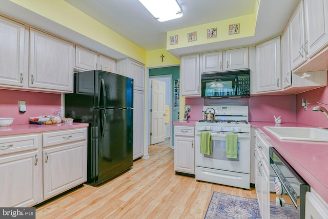 kitchen featuring light countertops, white cabinets, a sink, light wood-style flooring, and black appliances