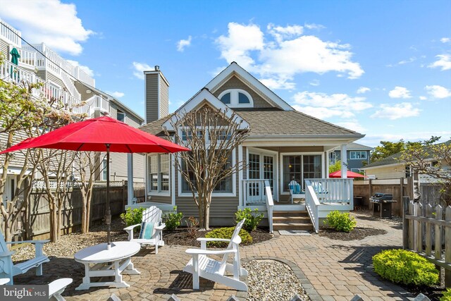 back of property with a fenced backyard, a wooden deck, a patio area, and roof with shingles