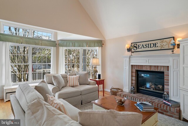 living area featuring high vaulted ceiling, baseboards, a fireplace, and light wood-type flooring
