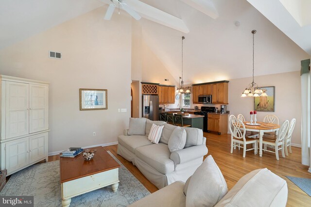 living room with baseboards, light wood-style flooring, ceiling fan with notable chandelier, and high vaulted ceiling