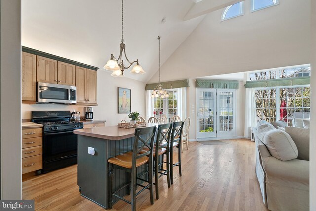 kitchen with gas stove, high vaulted ceiling, stainless steel microwave, an inviting chandelier, and a breakfast bar