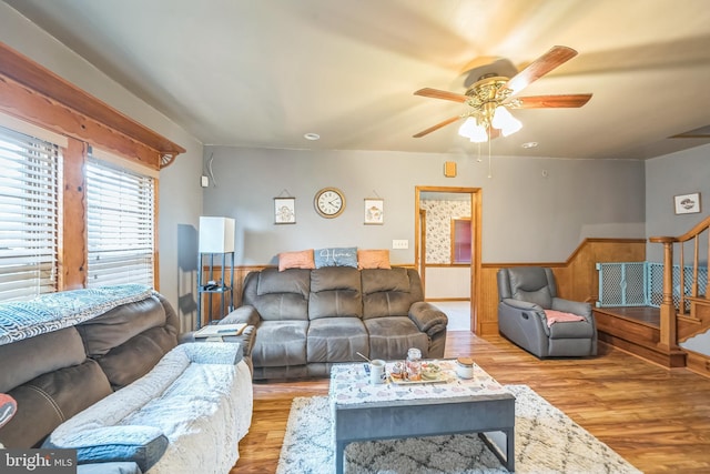 living room with a ceiling fan, wood finished floors, stairway, and a wainscoted wall