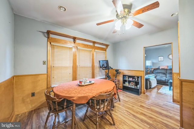 dining space with ceiling fan, wood finished floors, and a wainscoted wall