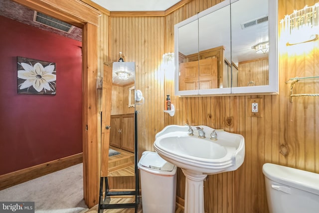 half bath featuring wooden walls, baseboards, toilet, and visible vents