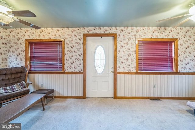 carpeted foyer featuring a wainscoted wall, ceiling fan, wallpapered walls, and visible vents