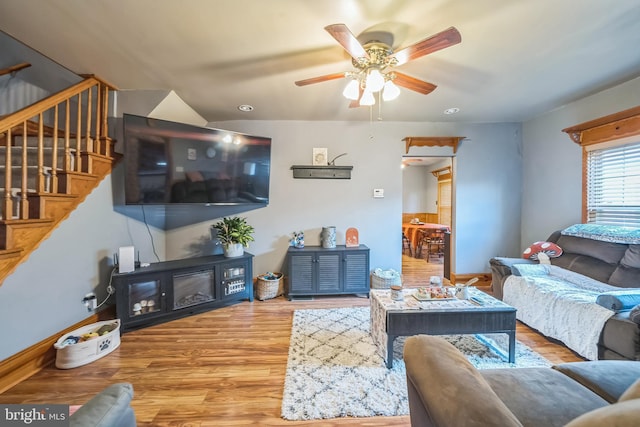 living room with stairs, a ceiling fan, baseboards, and wood finished floors